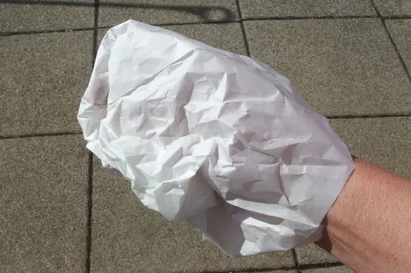 Eine Hand hält einen zerknüllten weißen Handschuh, der auf einem belebten Gehweg in der Sonne liegt.