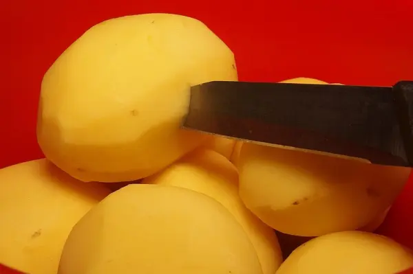 Messer sticht in geschälte Kartoffeln, die in einer roten Schüssel liegen, um das gleichmäßige Garen zu unterstützen.