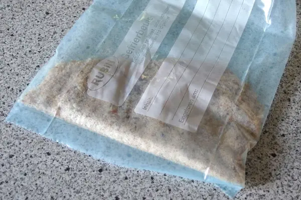Ein Gefrierbeutel enthält panierte Schnitzel. Darin wird gerade die Panade gleichmäßig verteilt. Der Untergrund ist eine Küchenarbeitsplatte.