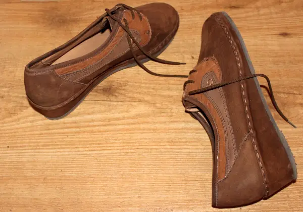 Stoff- und Wildlederschuhe liegen auf einem Holztisch, bereit zur Reinigung mit Polsterschaum.