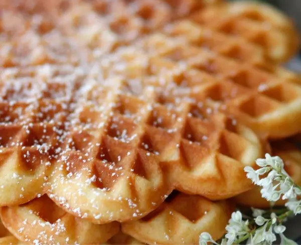 Nusswaffeln liegen appetitlich gestapelt, bestreut mit Puderzucker, umgeben von einer sanften, rustikalen Umgebung.