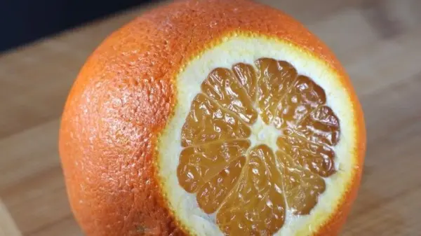 Eine orangefarbene Orange ist auf einem Holzbrett in der Mitte durchgeschnitten, wobei die fruchtigen Segmente sichtbar sind.