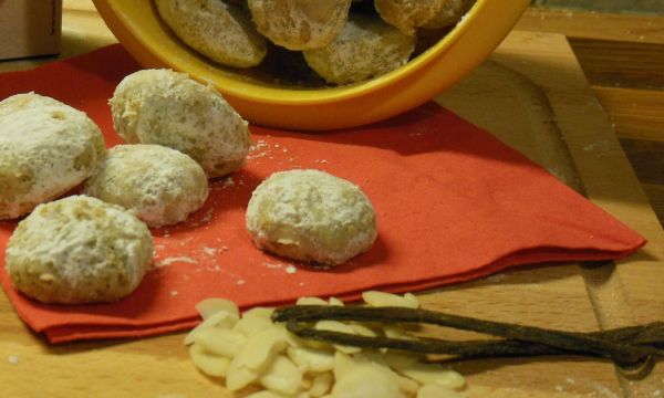 Kleine Vanillekipferl-Kugeln liegen auf einem roten Tuch, während weitere in einer gelben Schüssel im Hintergrund wohnen.
