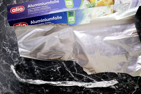 Alu-Papilotten werden vorbereitet, während eine Rolle Aluminiumfolie auf einer dunklen Oberfläche sichtbar ist.