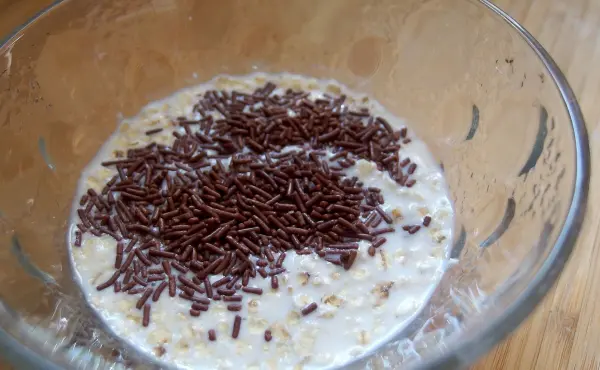 Eine Schüssel mit Haferflocken-Joghurt, bedeckt mit Schokoladenstreuseln, steht auf einem Holzuntergrund.
