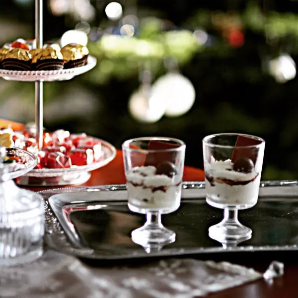 Zwei elegante Gläser mit Quark-Schmand-Creme und Sauerkirschen stehen auf einem Serviertablett vor einem festlichen Hintergrund.