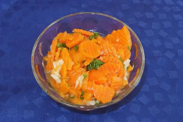 Ein bunter, gekochter Karottensalat in einer Schüssel liegt auf einem blauen Tisch und wartet auf das Servieren.