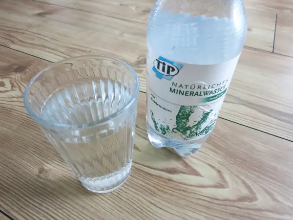Ein Glas mit kaltem Mineralwasser steht neben einer Flasche auf einem Holzfußboden, ideal zur Linderung von Zahnschmerzen.