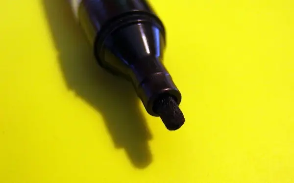 Ein schwarzer Edding-Marker liegt auf einem gelben Hintergrund, bereit, um auf einem Whiteboard verwendet zu werden.