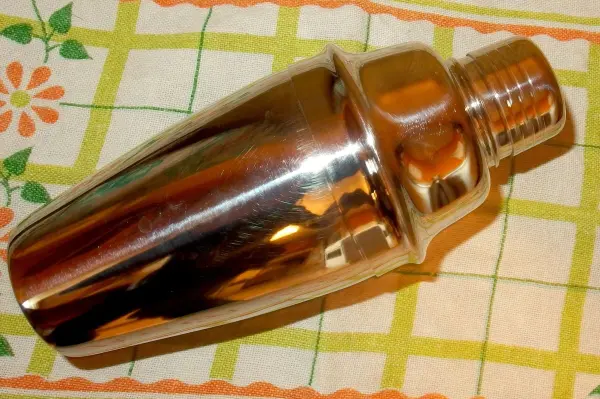 Ein Cocktailshaker liegt auf einem karierten Küchentuch und scheint klemmen zu wollen, während er glänzt.