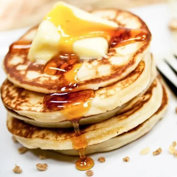 Stapel von American Pancakes, übergossen mit Sirup und einer Butterflocke, serviert auf einem weißen Teller.