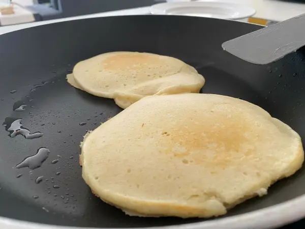 Zwei American Pancakes braten in einer Pfanne mit etwas Öl, während sie goldbraun werden und schön aufgegangen sind.