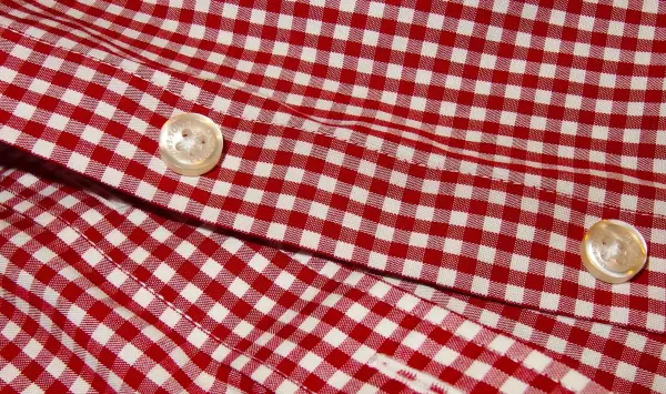 Zwei farblose Knöpfe auf einem rot-weiß karierten Hemd fixieren die Stofflagen, um ein einheitliches Design zu schaffen.