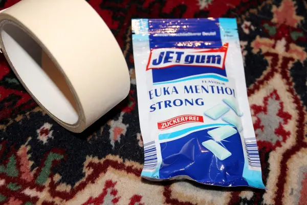Ein Beutel mit Kaugummi und ein Klebeband liegen auf einem bunten Teppich, was eine alltägliche Umgebung schafft.