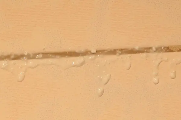 Wassertropfen stehen an einer Silikonfuge zwischen Fliesen, die möglicherweise Schimmelansätze zeigen.