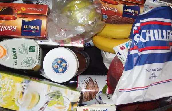 Ein bunter Mix aus Lebensmitteln liegt auf einer Fläche, darunter Bananen, Getränke und Snacks für die Einkaufsliste.