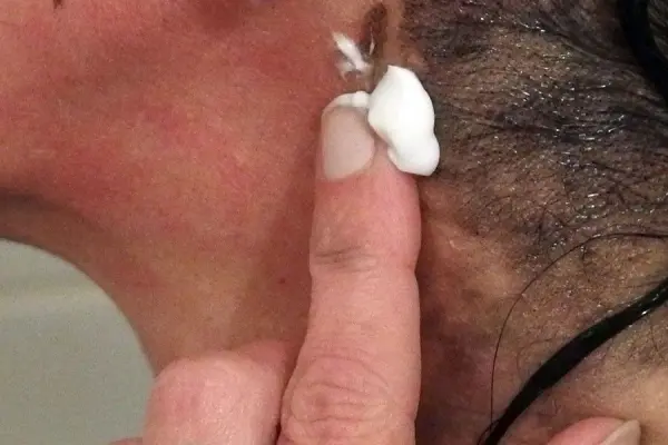 Eine Hand mit Zahnpasta berührt die Haut hinter dem Ohr, um Flecken nach dem Haarefärben zu entfernen.