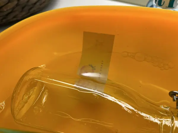 Ein Glas wird in einem orangefarbenen Reinigungsmittel eingeweicht, um Aufkleber und Klebereste zu entfernen.