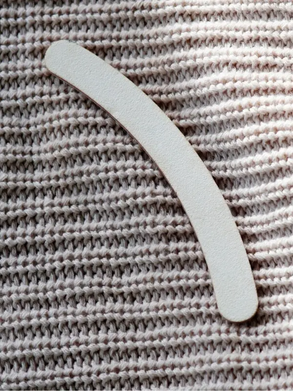 Eine Nagelfeile liegt auf einem gestreiften, grauen Stoff und eignet sich zum Entfernen von Fusseln.