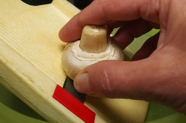Ein Champignon wird mit einer Hand gehalten, während er auf einem Schneidebrett fein geschnitten wird.