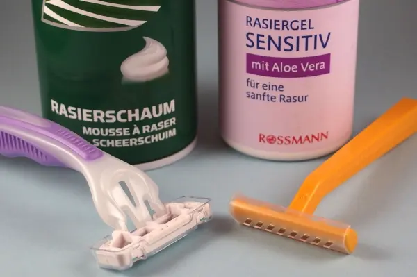 Ein Rasierer und ein Einwegrasierer liegen neben Rasiergel und -schaum im Badezimmer, bereit für eine gründliche Rasur.