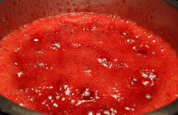 Leuchtend rote Erdbeermarmelade kocht sprudelnd in einem Topf, umgeben von einer gemütlichen Küchenatmosphäre.