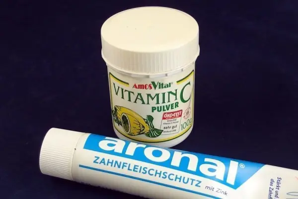 Ein Behälter mit Vitamin C-Pulver steht neben einer Zahnpasta, die für Zahnfleischschutz beworben wird.
