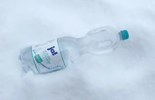Eine Wasserflasche liegt in frischem Schnee und verdeutlicht, wie man Strom sparen im Kühlschrank im Winter kann.