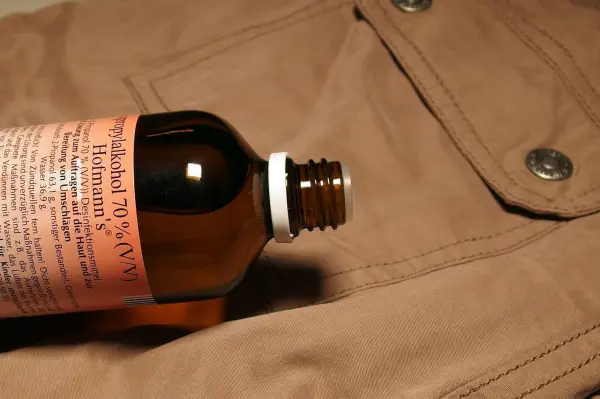 Eine braune Jacke liegt flach, während eine Flasche mit Reinigungslösung für Teerflecken darauf positioniert ist.