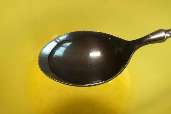 Ein Löffel steht auf einer gelben Oberfläche, während Eischnee in der Nähe geschlagen wird, um die Menge zu verdoppeln.