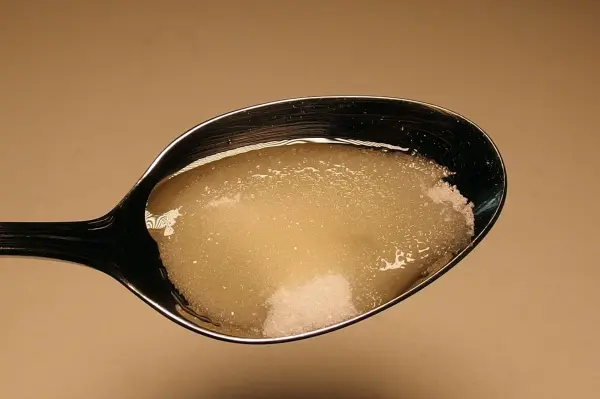Ein Löffel mit einem süßlichen Sirup und Zucker liegt vor einem hellen Hintergrund, um Linderung bei starkem Husten in der Nacht zu bieten.