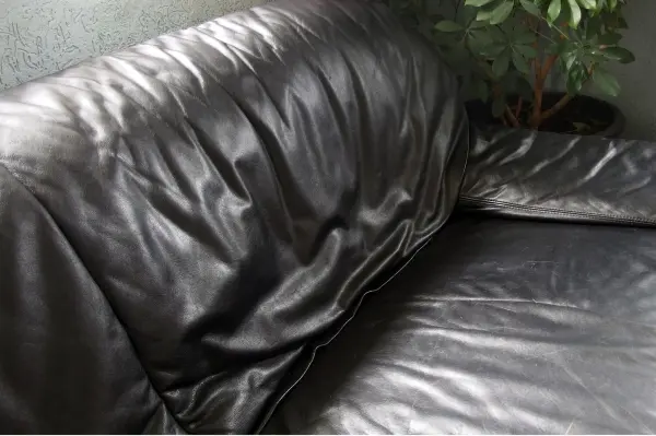 Ein schwarzes Ledersofa ruht in einer eleganten Umgebung, die Polsterung ist leicht zerknittert und glänzend.