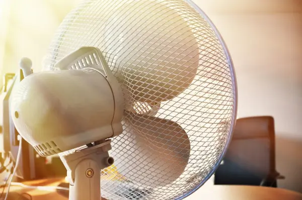 Ventilator dreht sich in einem Büroraum und sorgt für Luftzirkulation. Sunschein beleuchtet den Raum hinter dem Gerät.