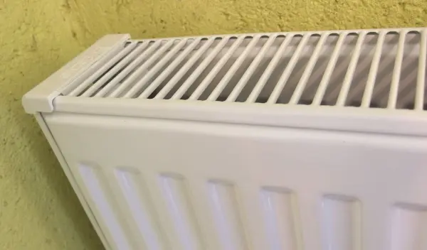 Ein Heizkörper steht an einer gelben Wand. Er ist sauber und bereit für die Reinigung von Staub mit einem Dampfreiniger.