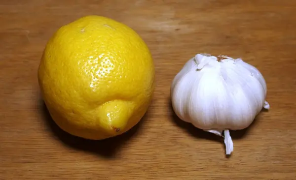 Eine frische Zitrone und eine Knoblauchzehe liegen auf einem Holzuntergrund, bereit für ein gesundes Zitronenknoblauchgetränk.