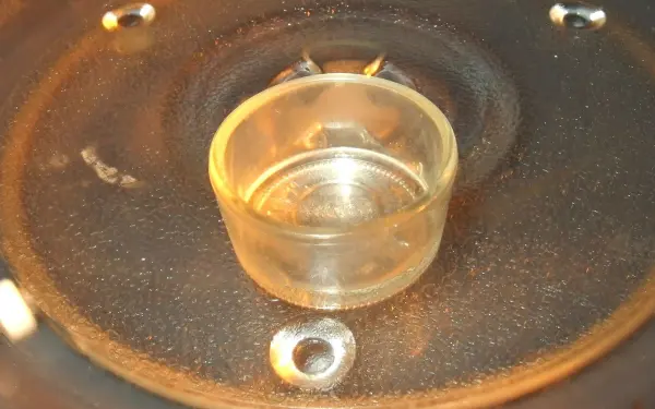 Ein transparenter Behälter steht in einer Mikrowelle, während er Kerzenwachs erhitzt, um es zu entfernen.