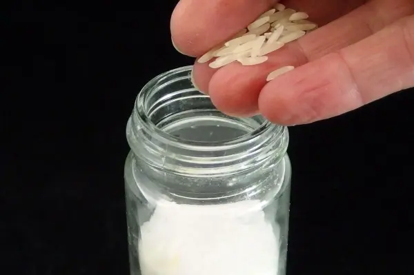 Eine Hand streut fein gemahlenes Salz aus einem Glas auf eine leichte Oberfläche, während der dunkle Hintergrund scharf kontrastiert.