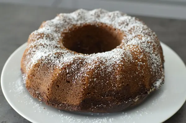 Ein Gugelhupf, aus Marmor mit Eierlikör, steht auf einem weißen Teller und ist mit Puderzucker bestäubt.