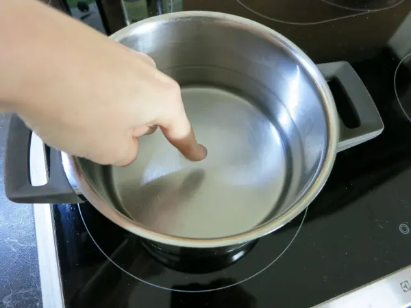 Ein Finger zeigt auf Wasser in einem Topf auf einem Herd, während das Wasser erhitzt wird. Wann ist Wasser gar?
