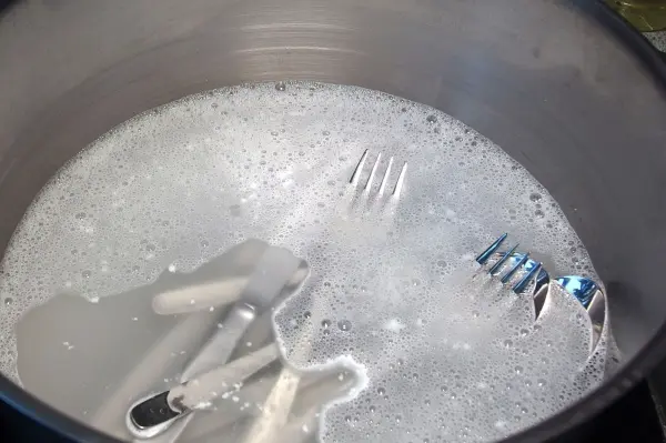 Glänzendes Besteck liegt in einem Topf mit schäumendem Wasser und Waschpulver, das zum Reinigen vorbereitet ist.