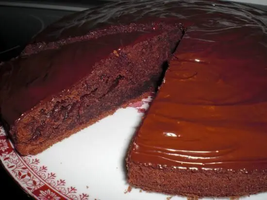 Ein Stück Schokokuchen wird angeschnitten, ruht auf einem dekorativen Teller in einer Küche. Keine zusätzlichen Textelemente.