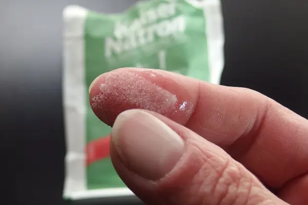 Ein Finger hält ein wenig Kaiser Natron Pulver, während eine Packung im Hintergrund sichtbar ist.