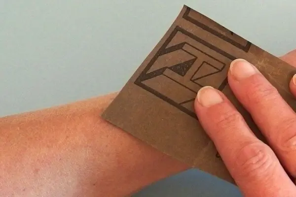 Eine Hand hält Schleifpapier und rubbelt damit über den Arm, um die Haarentfernung kostengünstig durchzuführen.