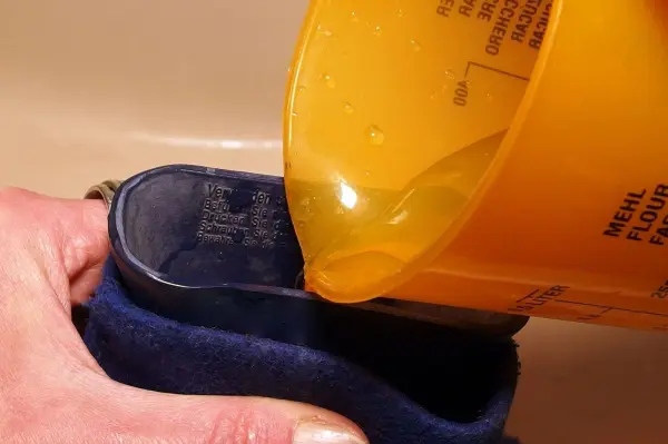 Eine Person füllt eine Wärmflasche mit heißem Wasser aus einem gelben Behälter, um sie warm zu halten.