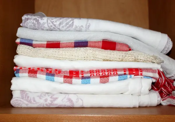 Gestapelte Tischdecken liegen ordentlich im Schrank und zeigen eine Mischung aus gemusterten und einfarbigen Designs.