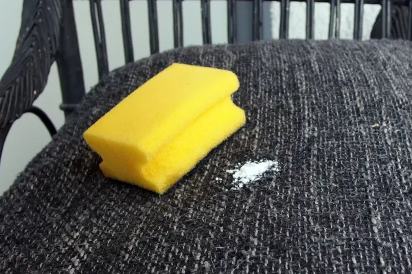 Ein gelber Schwamm liegt auf einem dunkelgrauen Polster, daneben ist etwas Waschpulver verstreut.