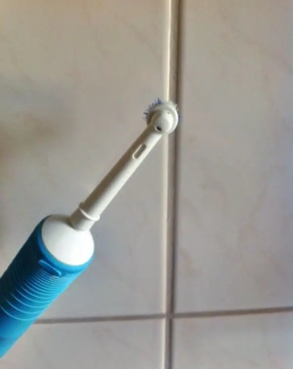 Eine elektrische Zahnbürste reinigt Badfugen auf einer gefliesten Wand mit hellen, beigen Fliesen.