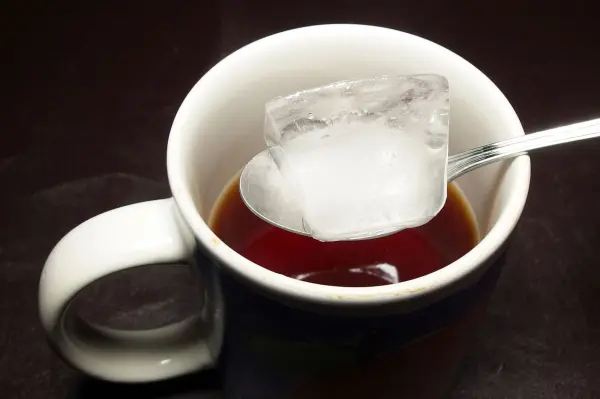Eine Tasse mit Tee und einem Eiswürfel darin, der schmelzend die Temperatur des Getränks senkt.