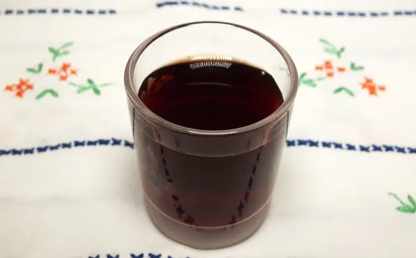 Ein Glas Pflaumenlikör steht auf einem gemusterten Tischset, umgeben von floralen Motiven auf dem Stoff.