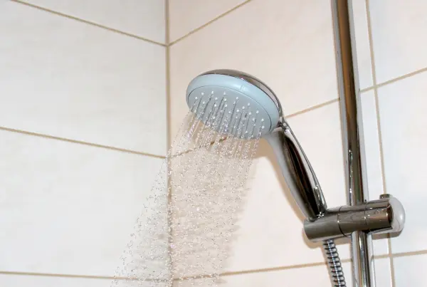 Ein Duschkopf sprüht Wasser in einem modernen Badezimmer. Der Fokus liegt auf dem Wasserverbrauch, um Ressourcen zu sparen.